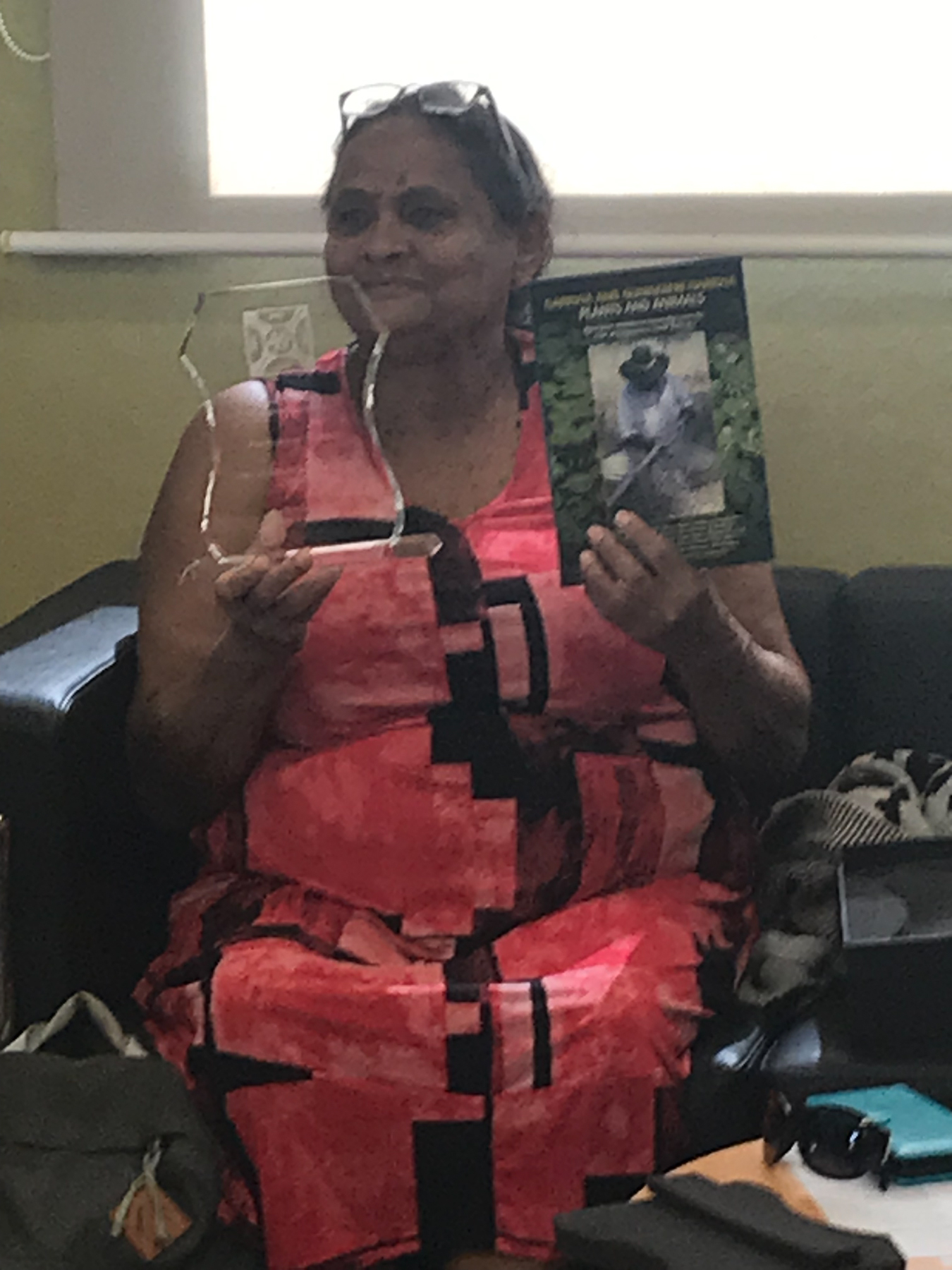 Daphne Mawson sitting down on a char, holding the Mrs Nakkamarra Nixon Award on her right hand, and the Garrwa Book on her left hand.